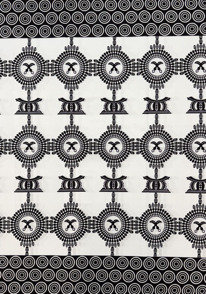 Black and white patterned fabric featuring a repeating geometric design with circular motifs and stylized central symbols, bordered by dense concentric circle bands at the top and bottom.